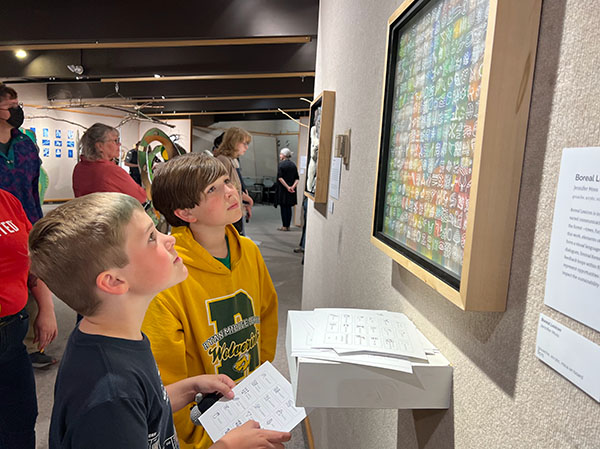 two children hold a paper with text and look up intently at a painting on a wall